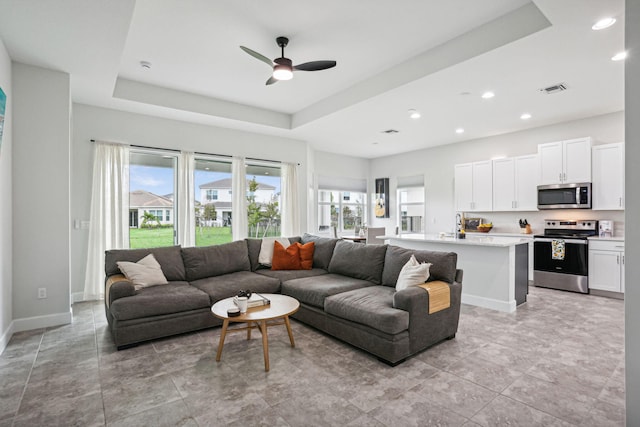 living room with a raised ceiling, ceiling fan, and plenty of natural light