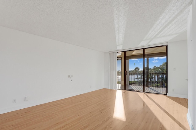 empty room featuring a textured ceiling, light hardwood / wood-style floors, and expansive windows