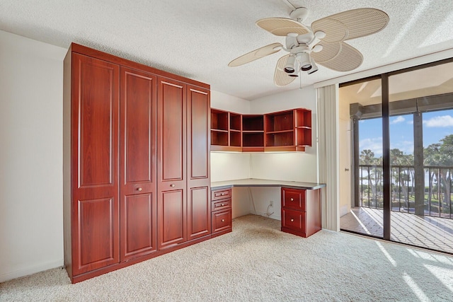 unfurnished office with ceiling fan, light colored carpet, built in desk, and a textured ceiling