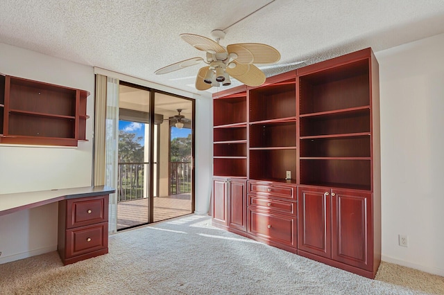 interior space with ceiling fan, light colored carpet, built in desk, and a textured ceiling