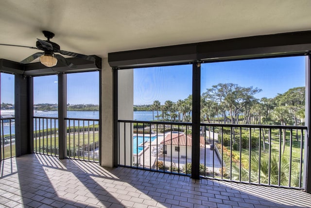 unfurnished sunroom featuring ceiling fan, a water view, and a wealth of natural light