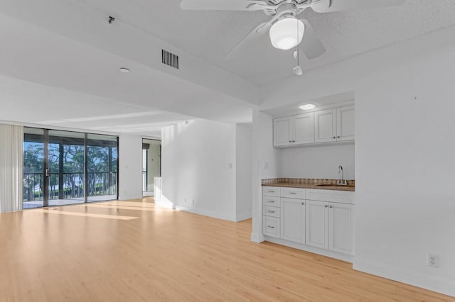 unfurnished living room featuring ceiling fan, sink, a wall of windows, light hardwood / wood-style flooring, and a textured ceiling