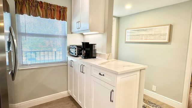 kitchen with white cabinets, stainless steel fridge with ice dispenser, light stone countertops, and a healthy amount of sunlight