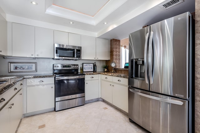 kitchen featuring appliances with stainless steel finishes, white cabinetry, a raised ceiling, and dark stone counters