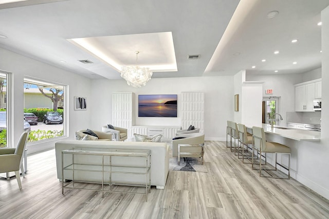 living room with a chandelier, light wood-type flooring, a raised ceiling, and sink