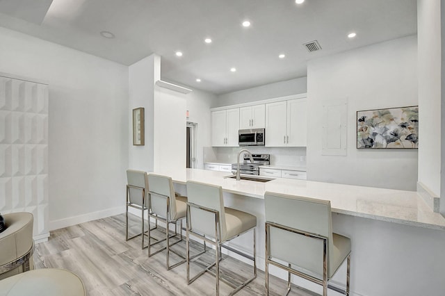 kitchen featuring a kitchen bar, kitchen peninsula, stainless steel appliances, sink, and white cabinetry