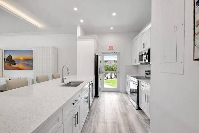 kitchen featuring sink, light stone countertops, appliances with stainless steel finishes, light hardwood / wood-style floors, and white cabinetry