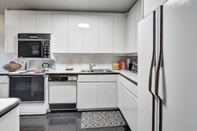 kitchen featuring white appliances, white cabinetry, dark tile patterned floors, and sink