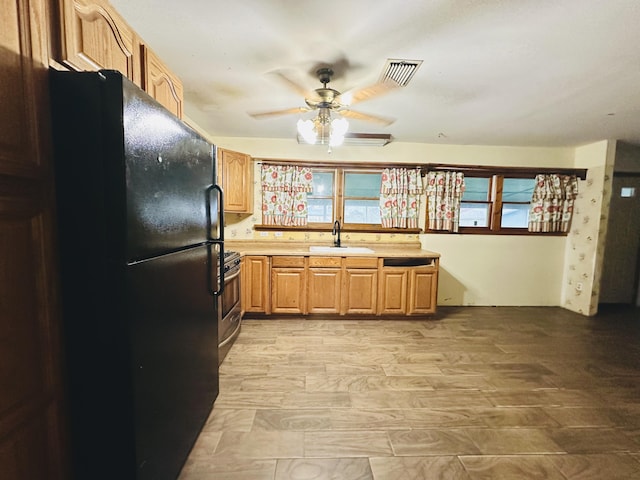 kitchen featuring sink, light hardwood / wood-style flooring, ceiling fan, gas stove, and black fridge