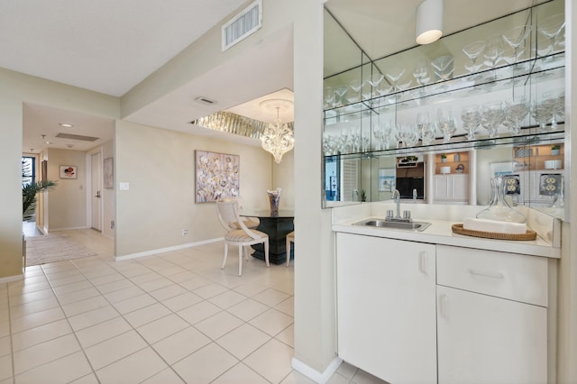 bar with white cabinetry, light tile patterned floors, sink, and a chandelier