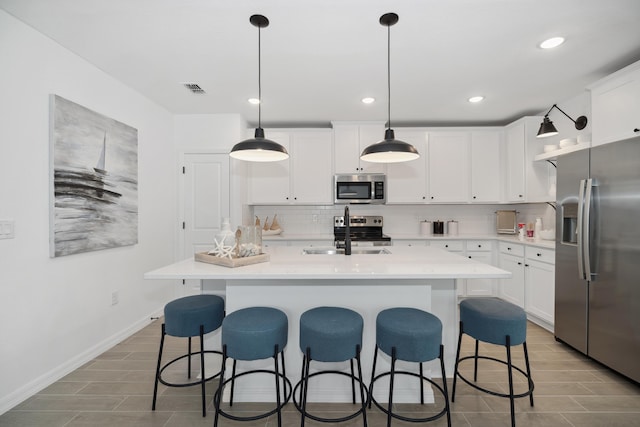 kitchen featuring white cabinets, decorative light fixtures, stainless steel appliances, and a center island with sink