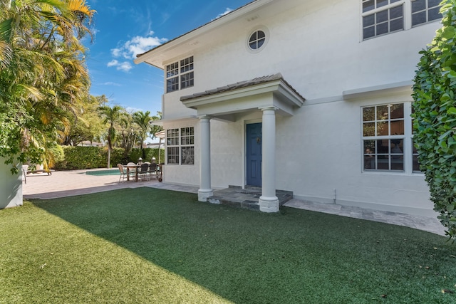 rear view of house with an outdoor pool, a patio area, a lawn, and stucco siding