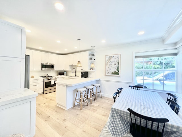 kitchen featuring stainless steel appliances, sink, pendant lighting, light hardwood / wood-style flooring, and white cabinets