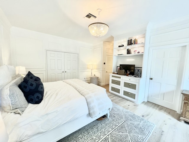 bedroom featuring a chandelier, a decorative wall, visible vents, light wood-style floors, and a closet