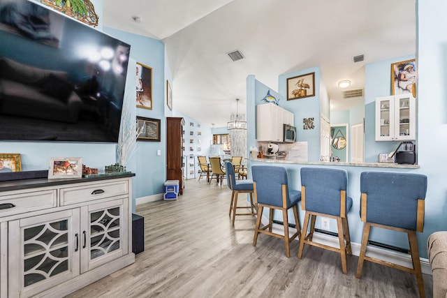 kitchen with a breakfast bar, vaulted ceiling, kitchen peninsula, light hardwood / wood-style floors, and white cabinets