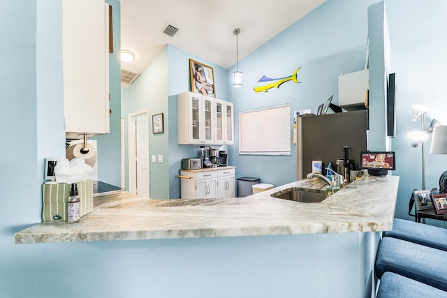 kitchen featuring pendant lighting, sink, lofted ceiling, white cabinetry, and kitchen peninsula