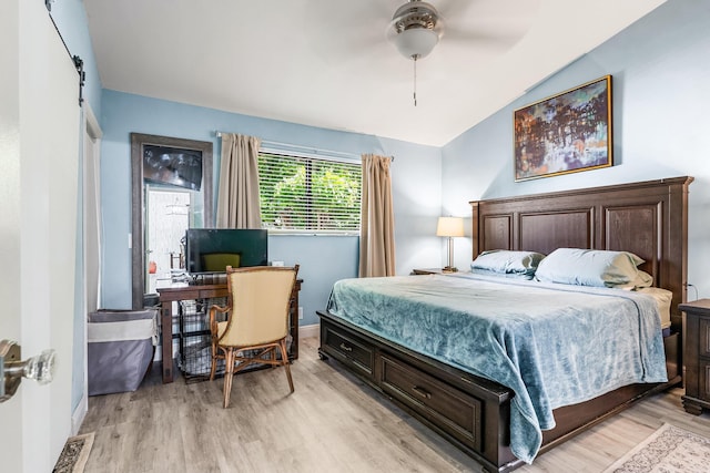 bedroom featuring ceiling fan, a barn door, vaulted ceiling, and light wood-type flooring