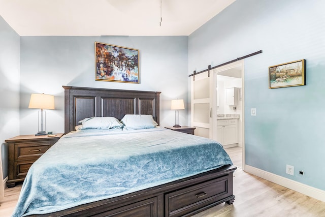 bedroom with a barn door, light hardwood / wood-style floors, and ensuite bath