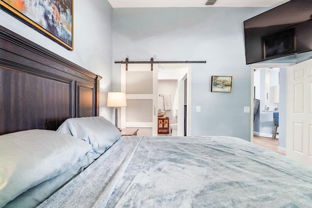 bedroom with ensuite bathroom, a barn door, and wood-type flooring