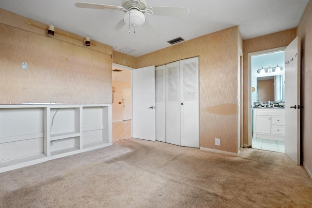 unfurnished bedroom featuring ensuite bathroom, ceiling fan, wooden walls, carpet floors, and a closet