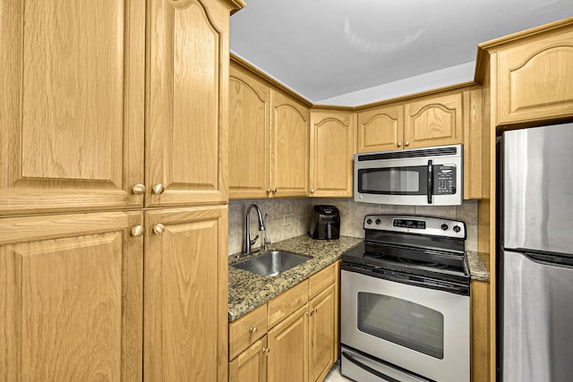 kitchen with stainless steel appliances, tasteful backsplash, light brown cabinetry, dark stone countertops, and sink