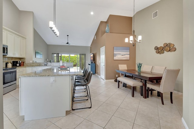 kitchen featuring appliances with stainless steel finishes, ceiling fan with notable chandelier, decorative light fixtures, and high vaulted ceiling