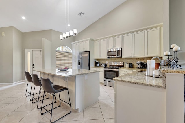 kitchen with sink, light stone counters, high vaulted ceiling, decorative light fixtures, and appliances with stainless steel finishes