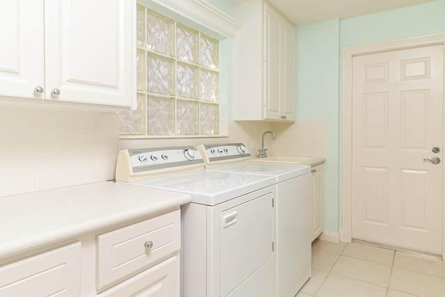 clothes washing area with washing machine and dryer, sink, light tile patterned flooring, and cabinets