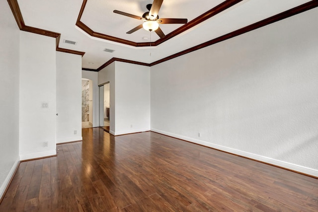 empty room with a raised ceiling, ceiling fan, dark wood-type flooring, and ornamental molding