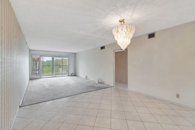 spare room featuring light colored carpet, a chandelier, and a textured ceiling