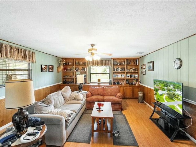 living room with wood-type flooring, plenty of natural light, wooden walls, and built in shelves