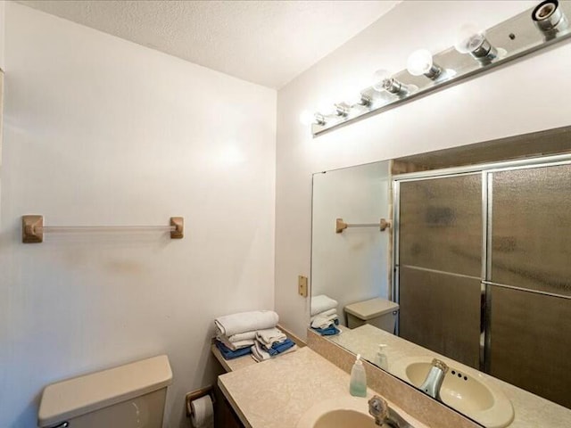 bathroom with toilet, a textured ceiling, a shower with door, and vanity