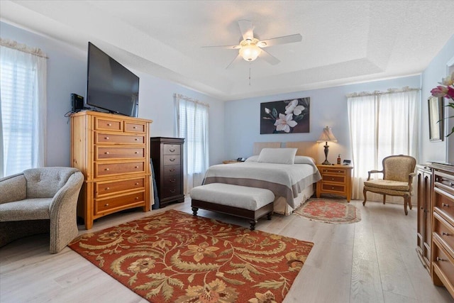 bedroom with light wood finished floors, a ceiling fan, and a tray ceiling