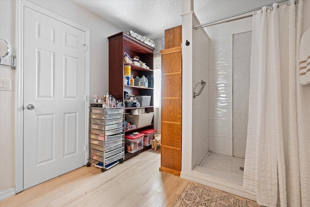 full bathroom with tiled shower, a textured ceiling, and wood finished floors