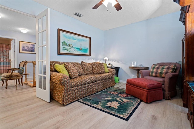 living room featuring ceiling fan, french doors, light hardwood / wood-style floors, and a textured ceiling