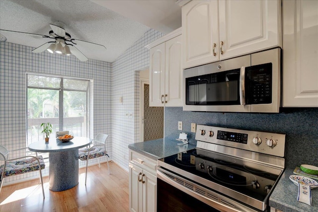 kitchen featuring a textured ceiling, stainless steel appliances, white cabinets, light hardwood / wood-style floors, and lofted ceiling