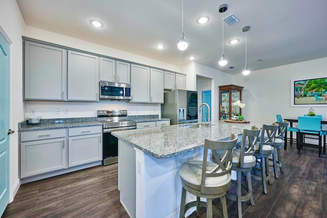 kitchen featuring sink, dark wood-type flooring, hanging light fixtures, stainless steel appliances, and a center island with sink