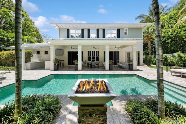 view of swimming pool with a patio, an outdoor kitchen, ceiling fan, and an outdoor living space with a fire pit