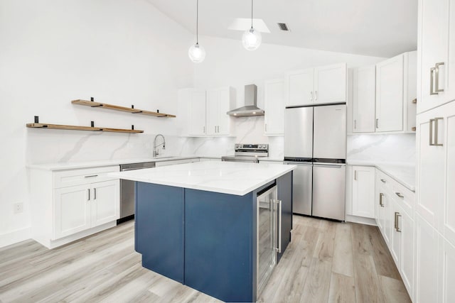 kitchen featuring white cabinets, a kitchen island, wall chimney range hood, and stainless steel appliances