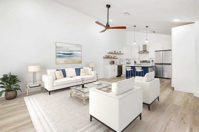 living room with ceiling fan, light hardwood / wood-style flooring, high vaulted ceiling, and sink