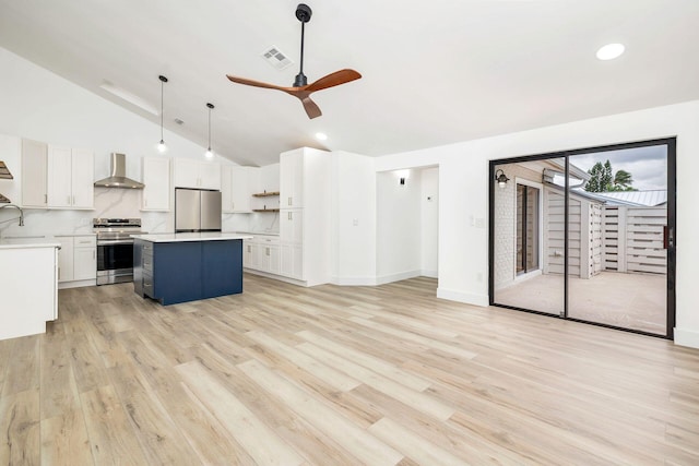 kitchen featuring wall chimney range hood, vaulted ceiling, decorative light fixtures, a kitchen island, and appliances with stainless steel finishes