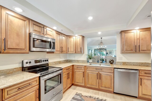 kitchen featuring appliances with stainless steel finishes, light stone counters, sink, a notable chandelier, and hanging light fixtures