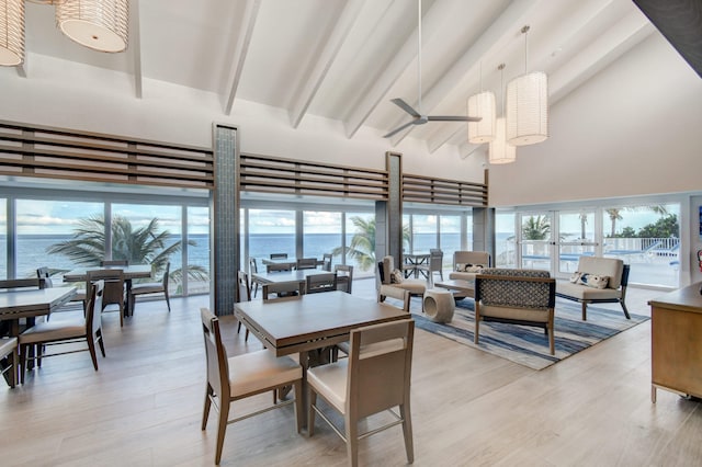 dining space with beam ceiling, ceiling fan, high vaulted ceiling, light hardwood / wood-style floors, and a water view