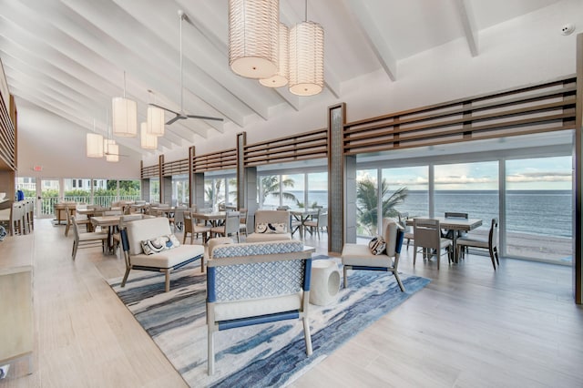 living room with beam ceiling, ceiling fan, light hardwood / wood-style flooring, high vaulted ceiling, and a water view