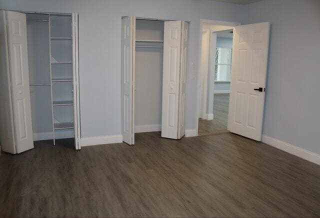 unfurnished bedroom with two closets and dark hardwood / wood-style floors