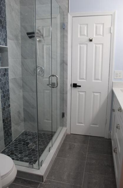 bathroom featuring tile patterned floors, vanity, a shower with shower door, and toilet