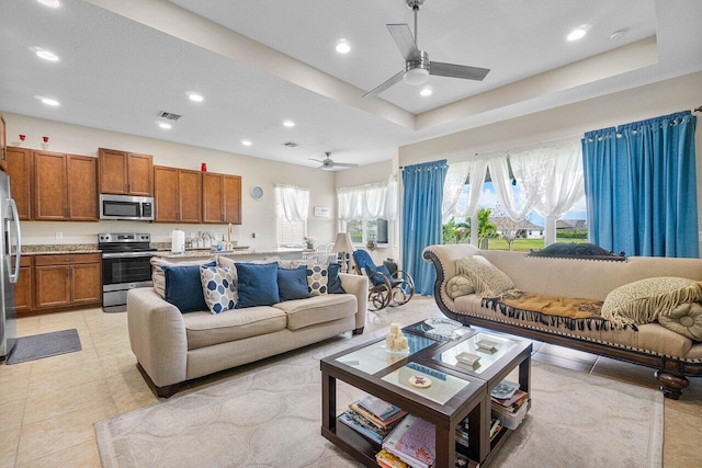 living room featuring a raised ceiling, ceiling fan, and light tile patterned floors