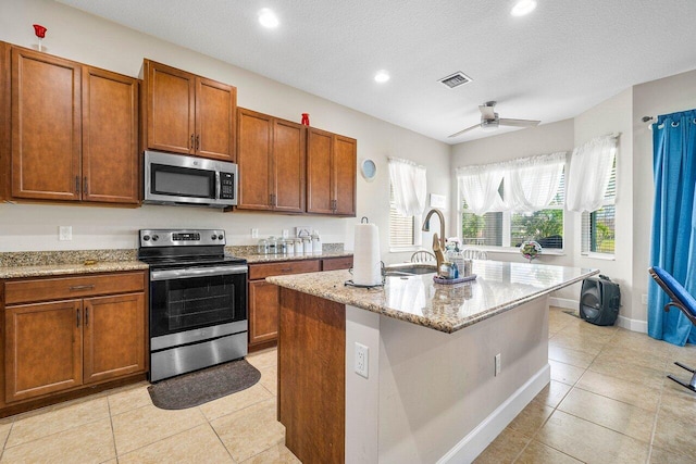 kitchen with sink, ceiling fan, a textured ceiling, an island with sink, and appliances with stainless steel finishes