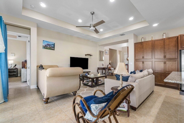 living room with a tray ceiling, ceiling fan, and light tile patterned flooring