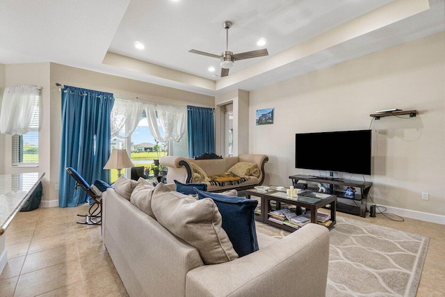 tiled living room with ceiling fan and a tray ceiling